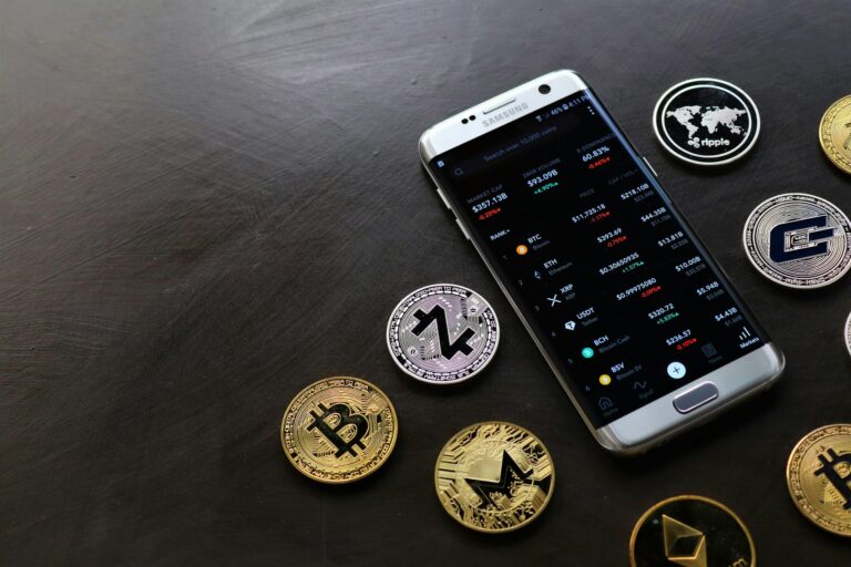 A collection of cryptocurrency coins and a smartphone displaying a digital trading platform.