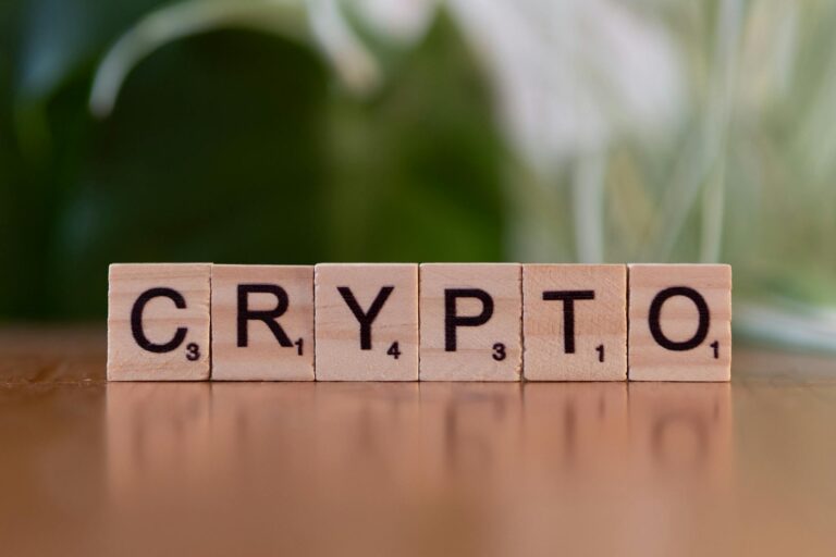 Wooden Scrabble tiles spelling 'CRYPTO' on a wooden surface with a blurred green background.